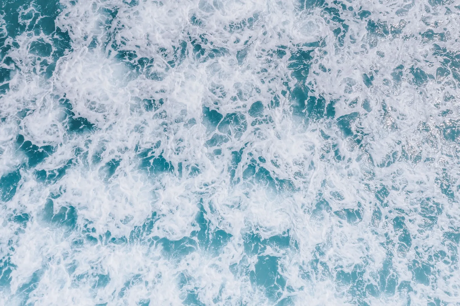 A dynamic top view of ocean waves and sea foam demonstrating nature's power and beauty.