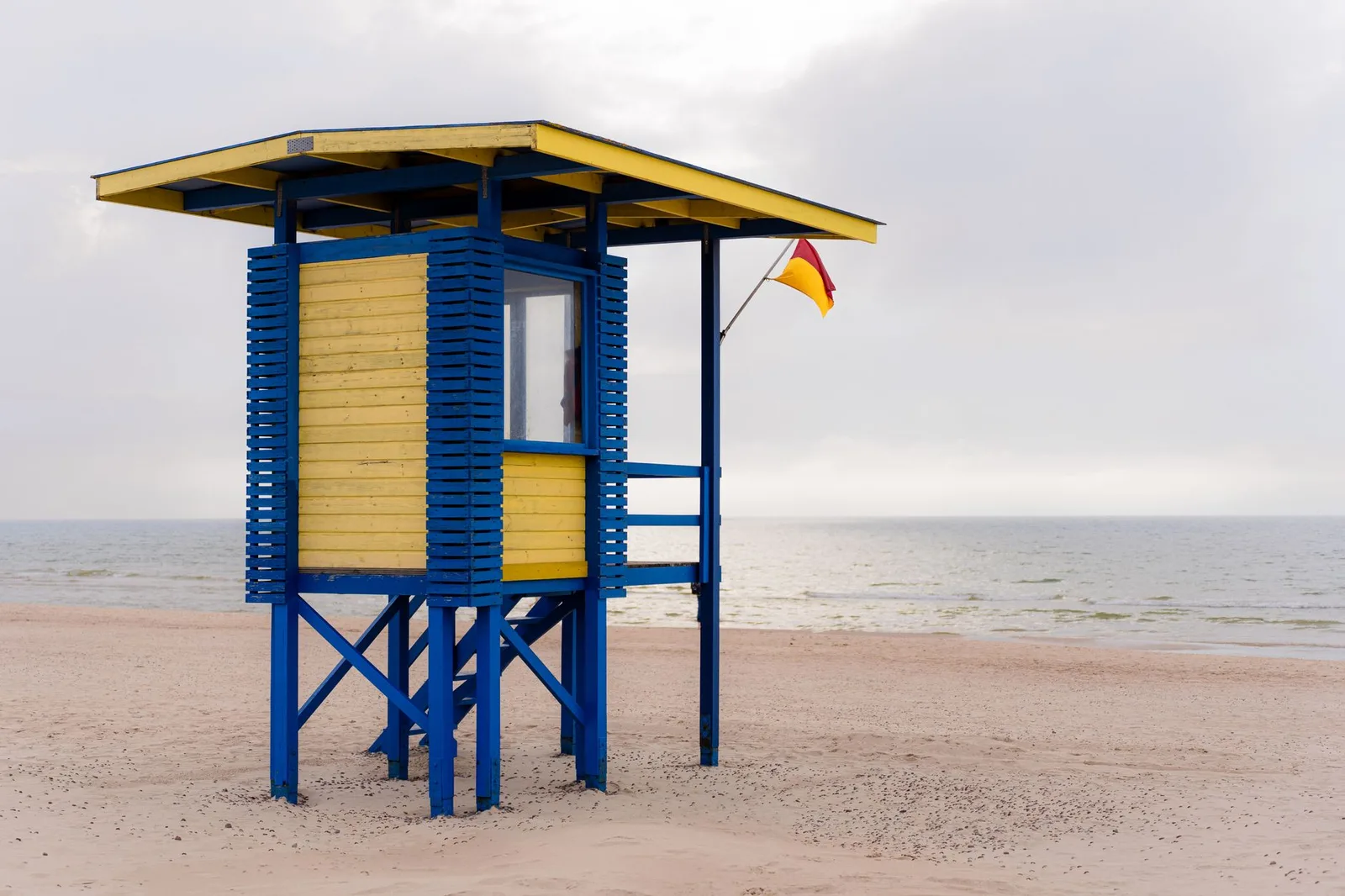Bright yellow and blue lifeguard tower overlooking a calm sandy beach with a flag visible.