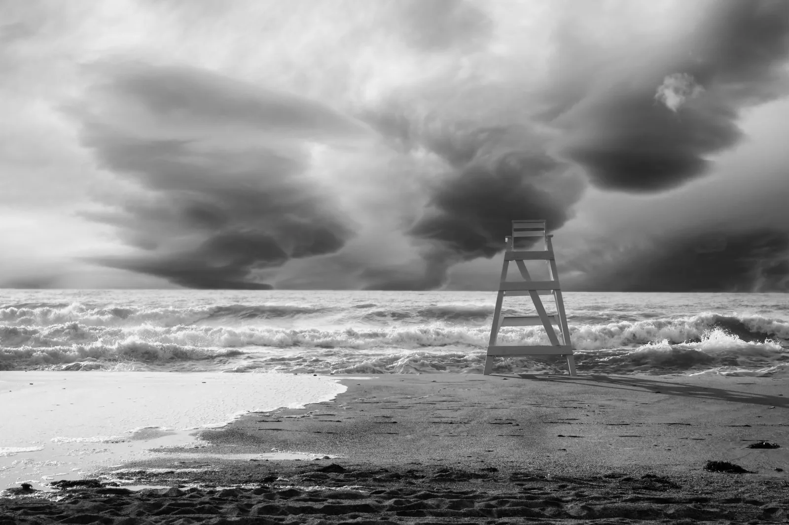 Black and white photo of a lifeguard tower on a stormy beach with dark clouds.