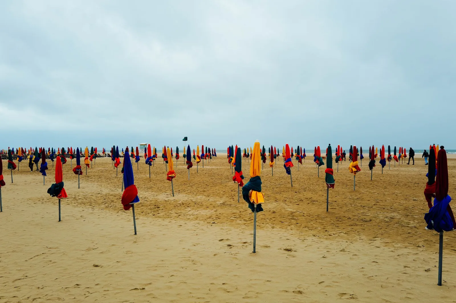 Rows of vibrant umbrellas stand ready on the sandy Deauville beach under cloudy skies.