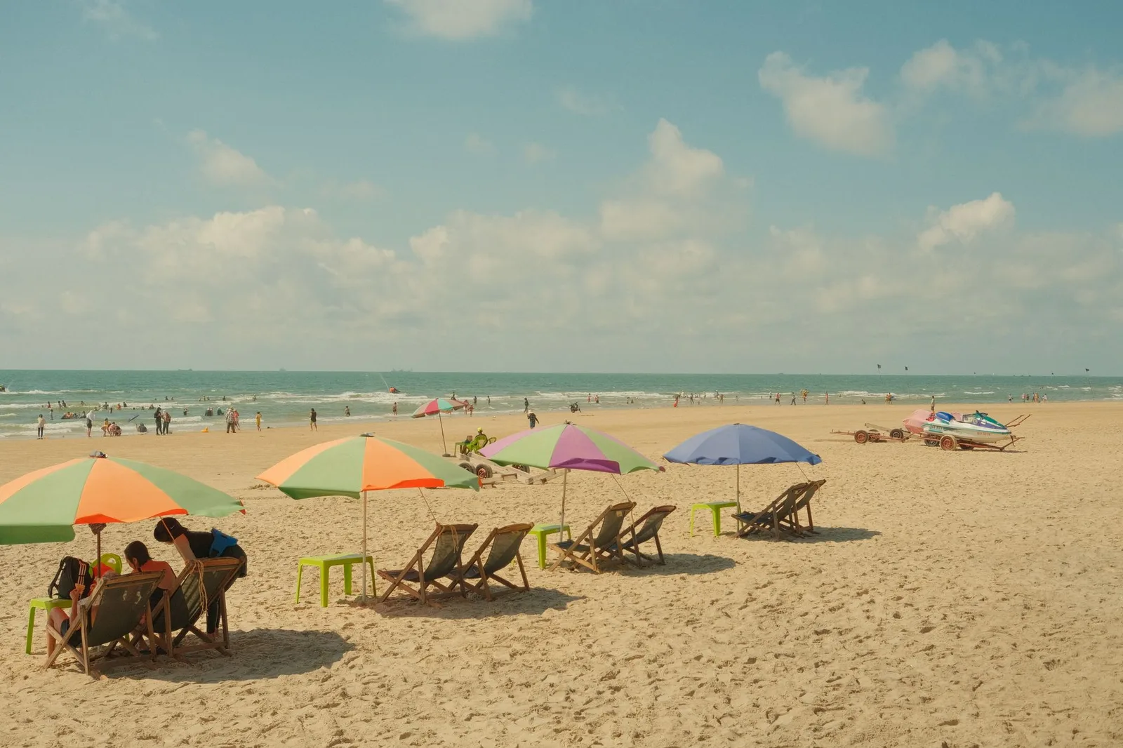 Scenic beach with colorful umbrellas, chairs, and people enjoying a sunny day.
