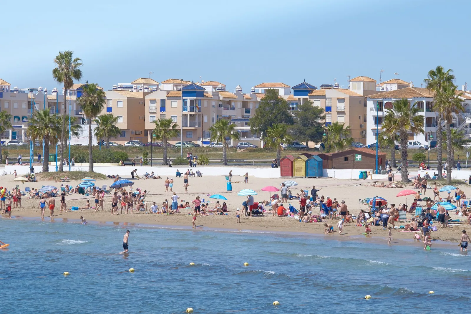 Enjoy a lively summer day at a bustling Mediterranean beach with people enjoying the sunshine.