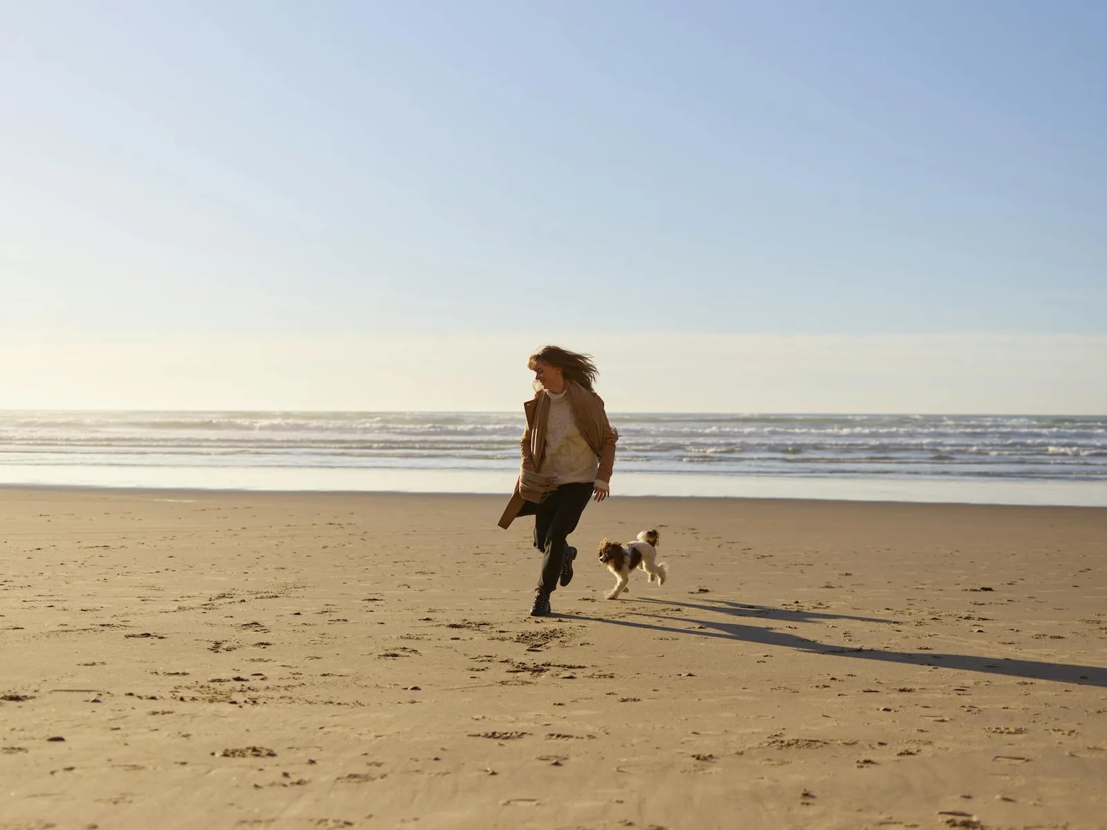 A joyful scene of a woman running with her dog on a sunny beach, capturing carefree fun.